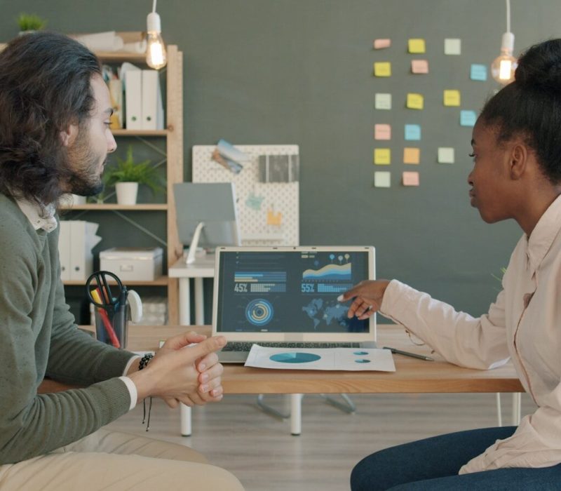 Two colleagues discussing data on a laptop screen.